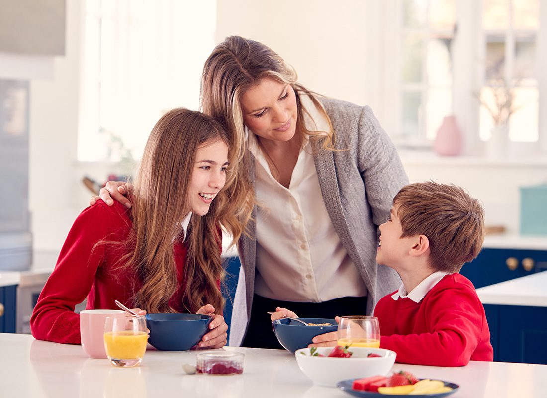 Personal Insurance - Happy Mother Looks at Her Children as They All Have Breakfast Before Leaving the House for School and Work